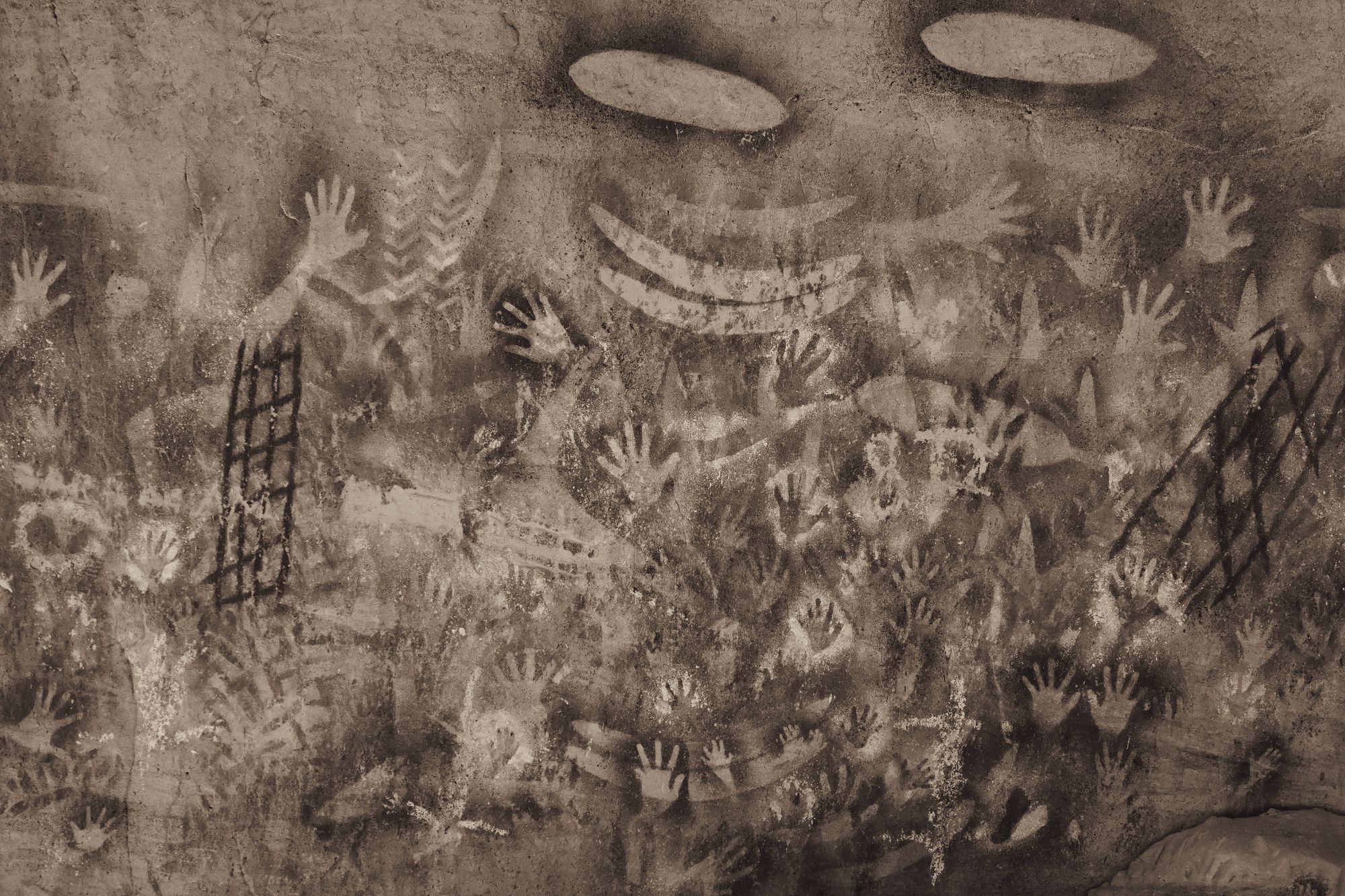 Layered ochre hand-stencil rock art covering a stone wall