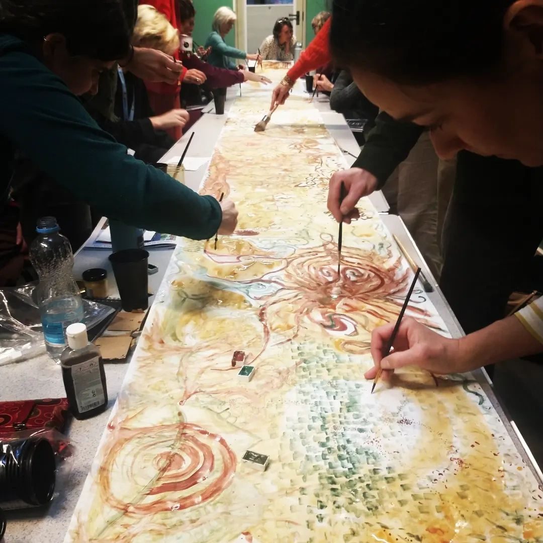 Workshop participants painting together with natural earth pigments on a long shared canvas