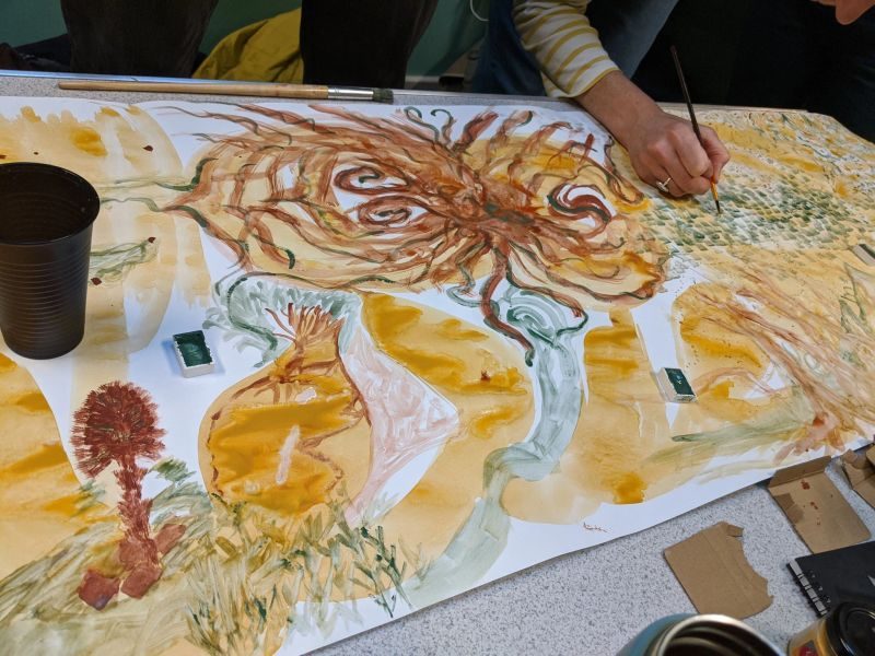 A participant painting swirling, root-like forms in ochre and sienna earth paint