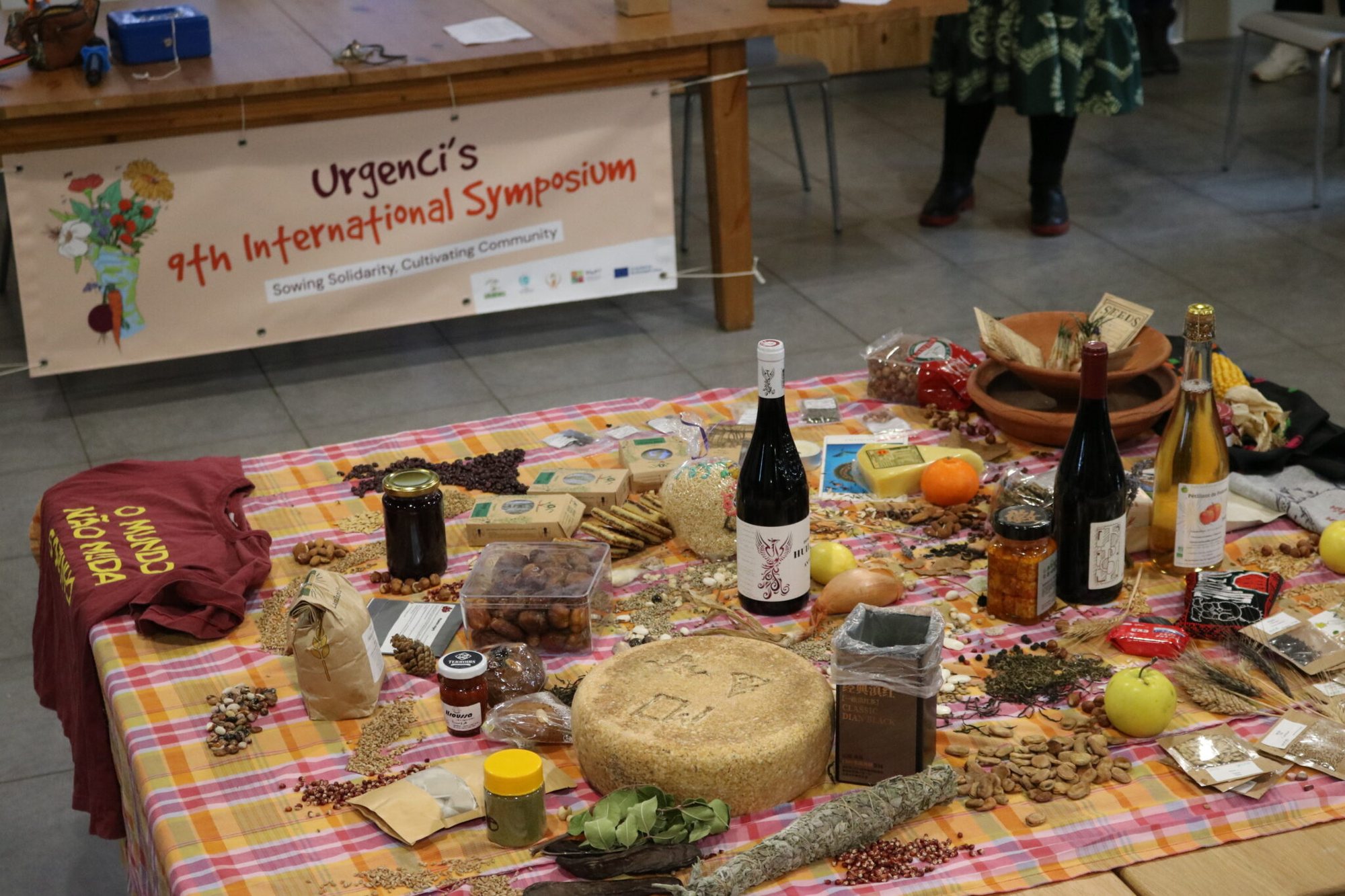 A table of seeds, breads, wines and local produce beneath the Urgenci 9th International Symposium banner